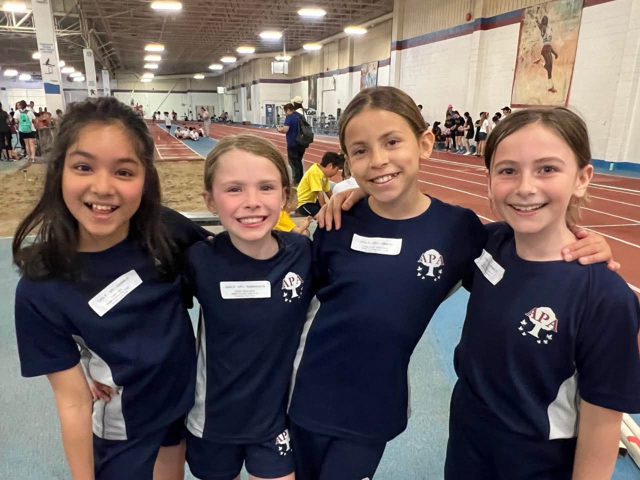 Four girls in APA track uniforms at an indoor meet