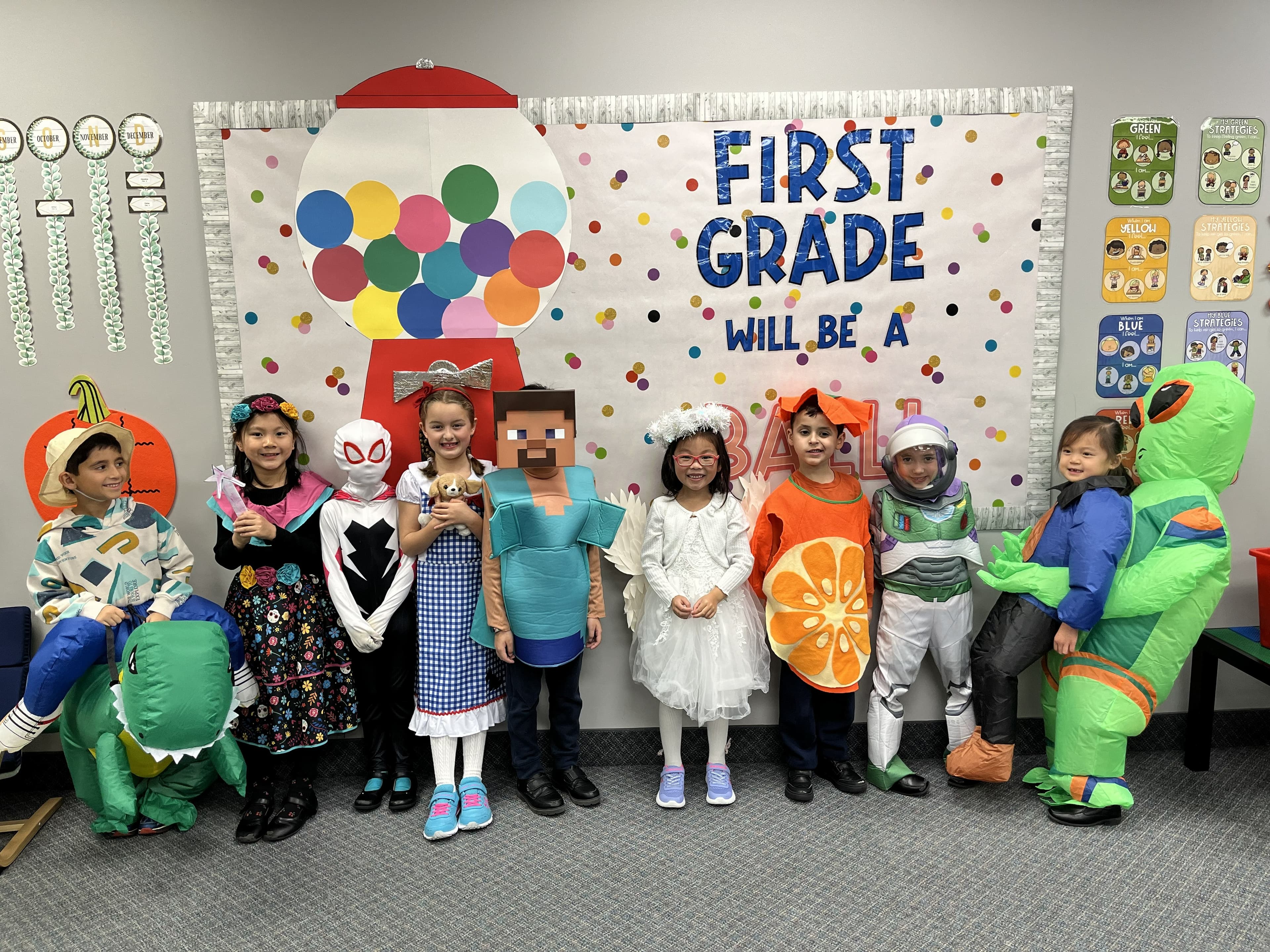 Grade 1 students in Halloween costumes in front of a colorful bulletin board