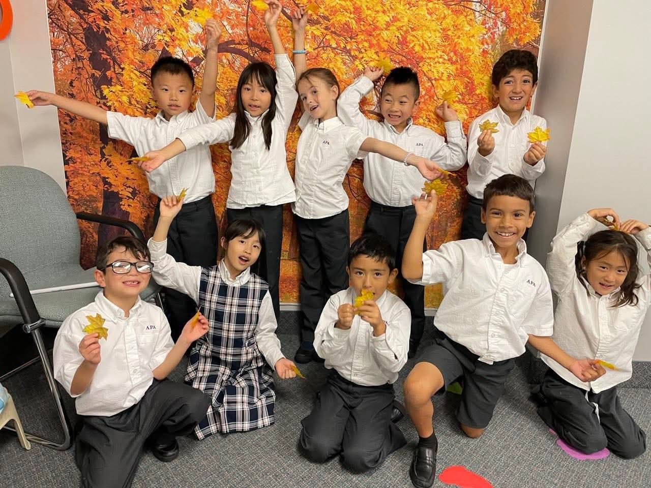 Students celebrating autumn with maple leaves in white APA uniforms